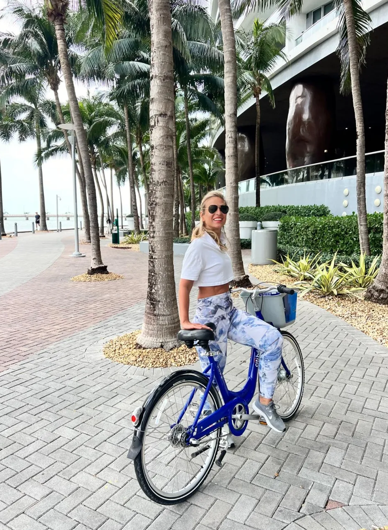 Founder of Haus of V outdoors with a bicycle beneath palm trees