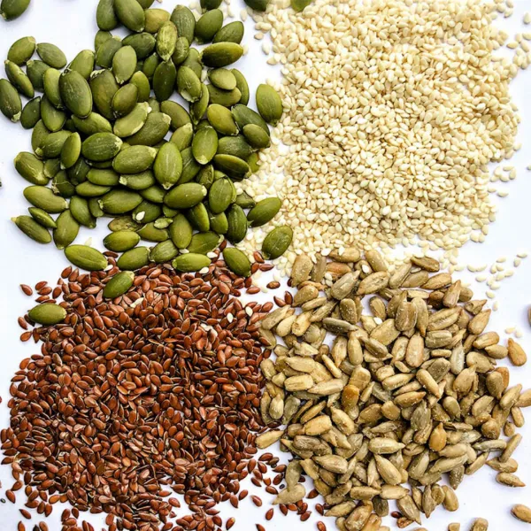 Flax, pumpkin, sesame, and sunflower seeds arranged in piles on a white surface
